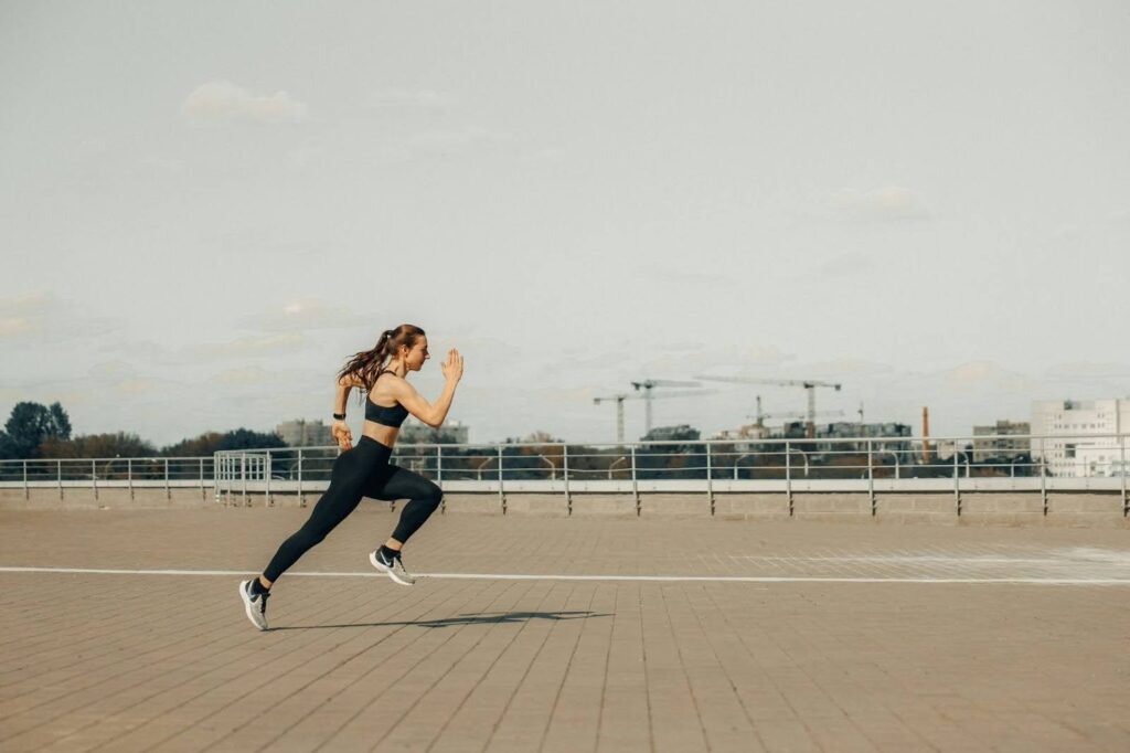 Female athlete sprinting on an outdoor track, showcasing the power and intensity of endurance athletes and underscoring how cutting out carbs can impact performance, recovery nutrition, and increase the risk of female overtraining symptoms.