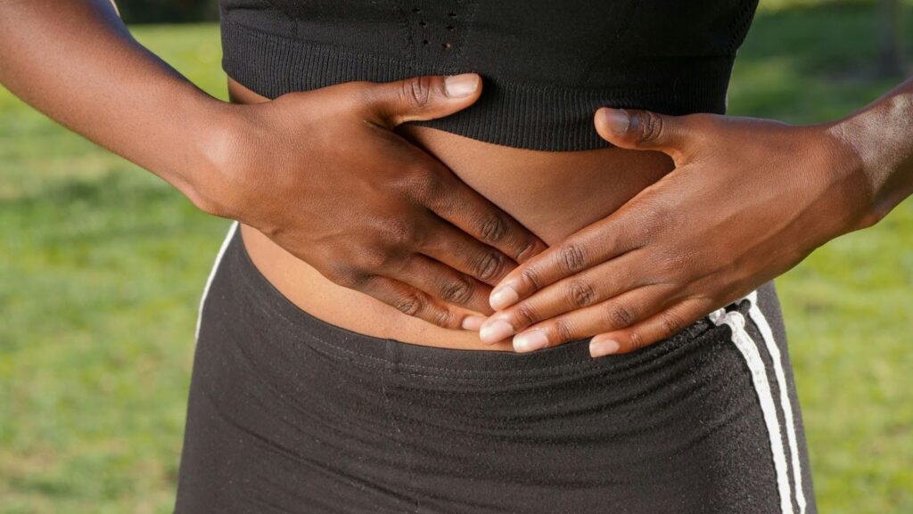 Close-up of a person holding their stomach while wearing workout clothes, illustrating GI distress, runner’s stomach, and the connection between exercise and digestion — highlighting gut training for managing exercise induced gastrointestinal distress.