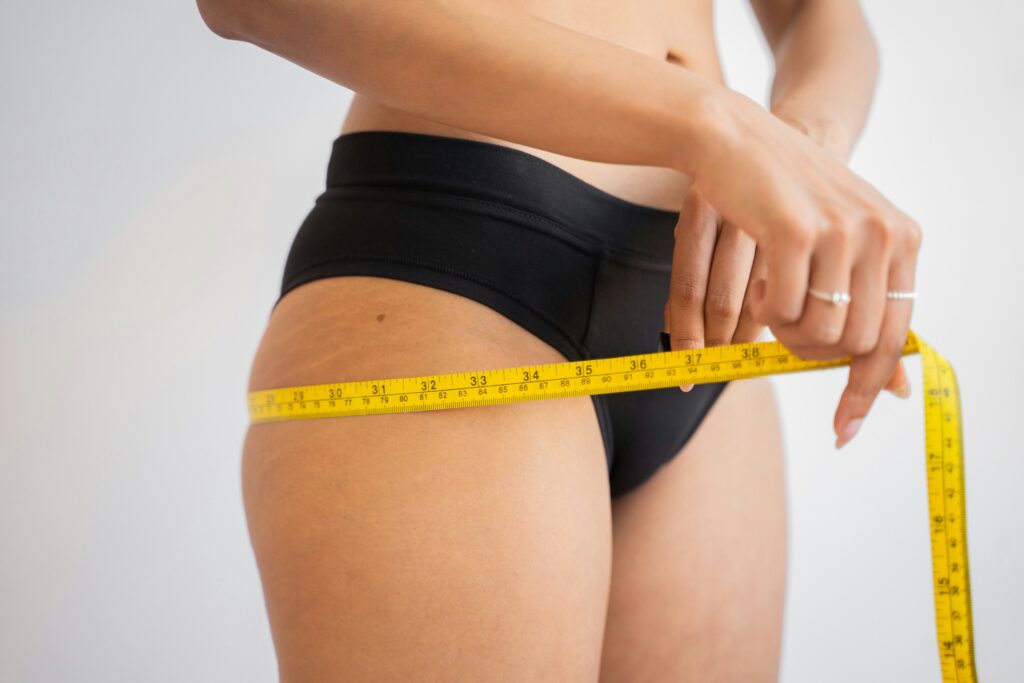 Close-up of an athlete measuring her thigh with a tape measure, representing athlete body image concerns, underfueling in athletes, and the need to focus on eating for energy and performance rather than body measurements.