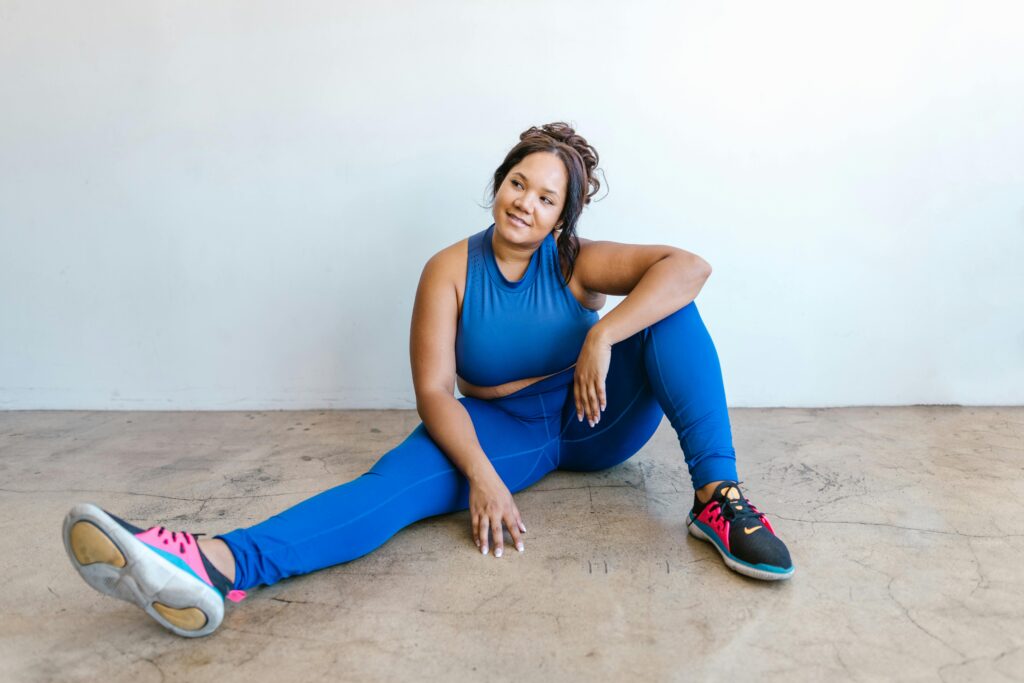 Endurance athlete seated on the gym floor in athletic wear, representing endurance athlete body diversity, strength, and a healthy nutrition mindset that values fueling and recovery over appearance.